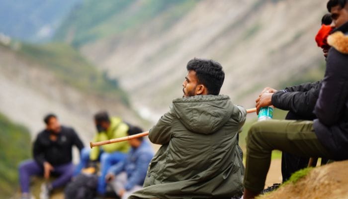 A male tourist resting on a mountain slope during a trek to Shri Kedarnath Temple, with scenic views of the Rudraprayag district in Uttarakhand, India